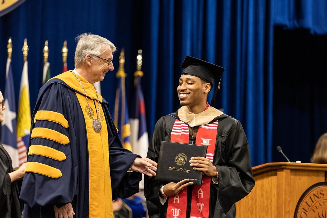 Rollins president handing diploma to Crummer graduate in full regalia. 