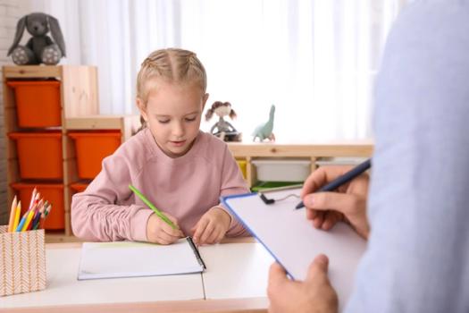 An applied behavior analyst takes notes as a young patient writes in a notebook.