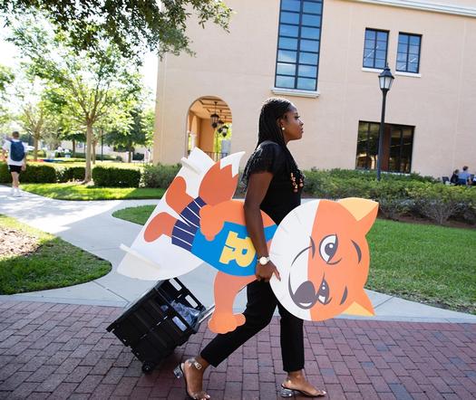 A Rollins student employee carries a fox mascot across campus.