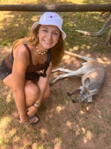 Smiling Rollins student crouches beside a resting kangaroo in a wildlife park.