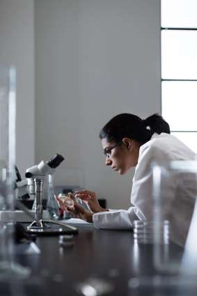 A college student wearing a lab coat working in a biology lab holding a petri dish.