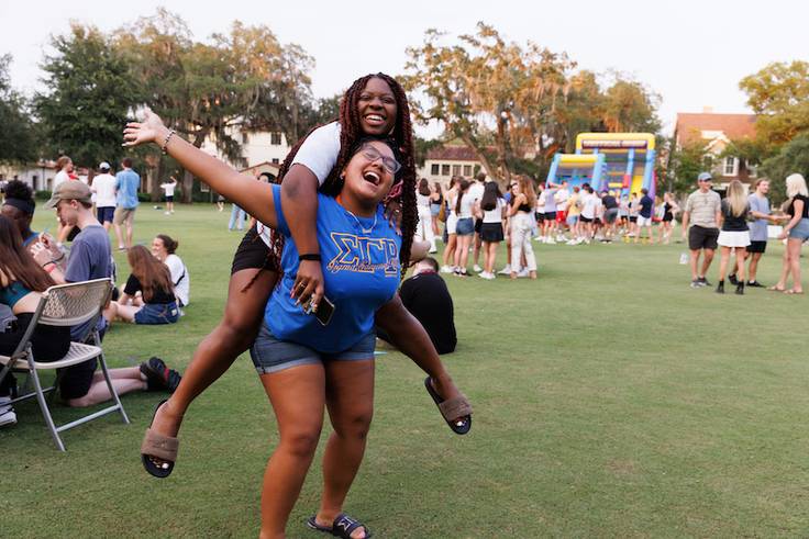 Two Rollins college students cheer while on the campus green. 
