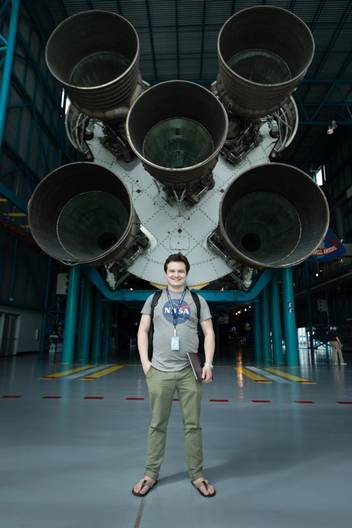 A student stands behind the first stage of a rocket at Kennedy Space Center.