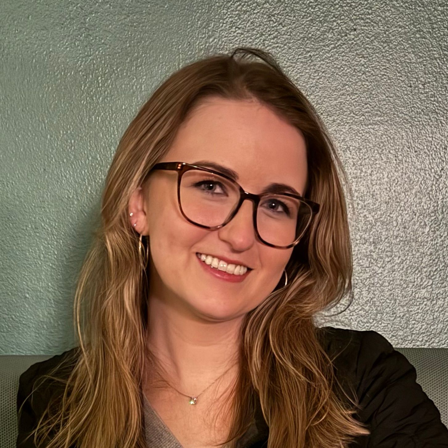 Smiling person with glasses posing against a textured green wall background.