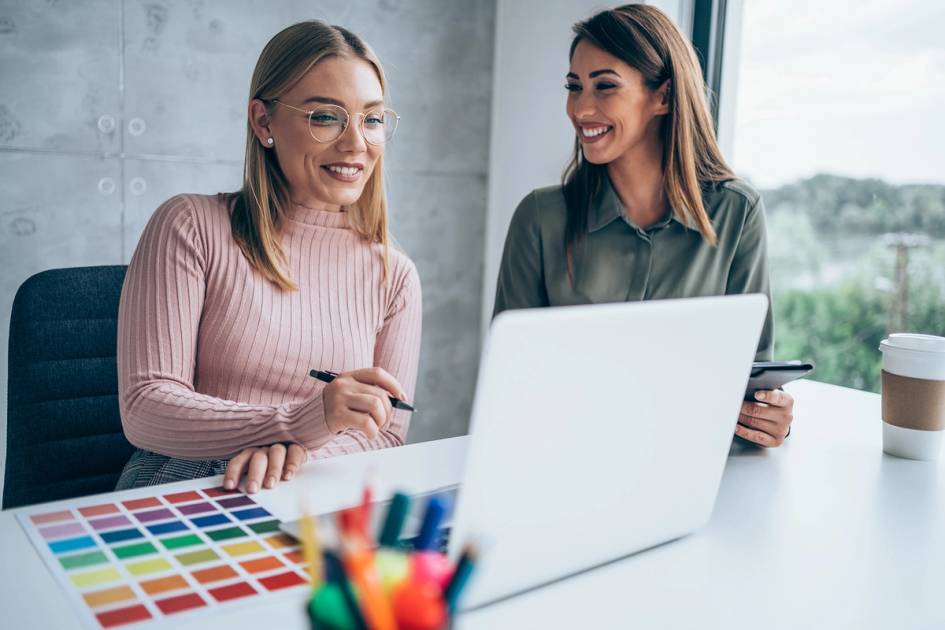 Two marketing professionals work on laptops in a sunny office.