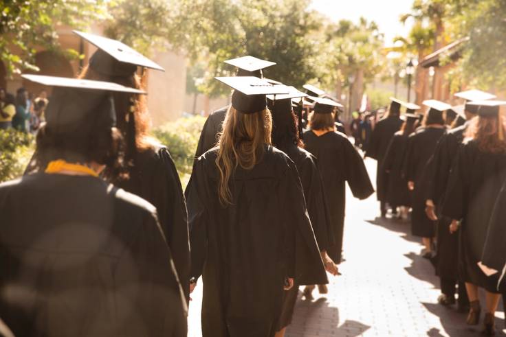 College graduates walk toward a commencement ceremony in cap and gown.