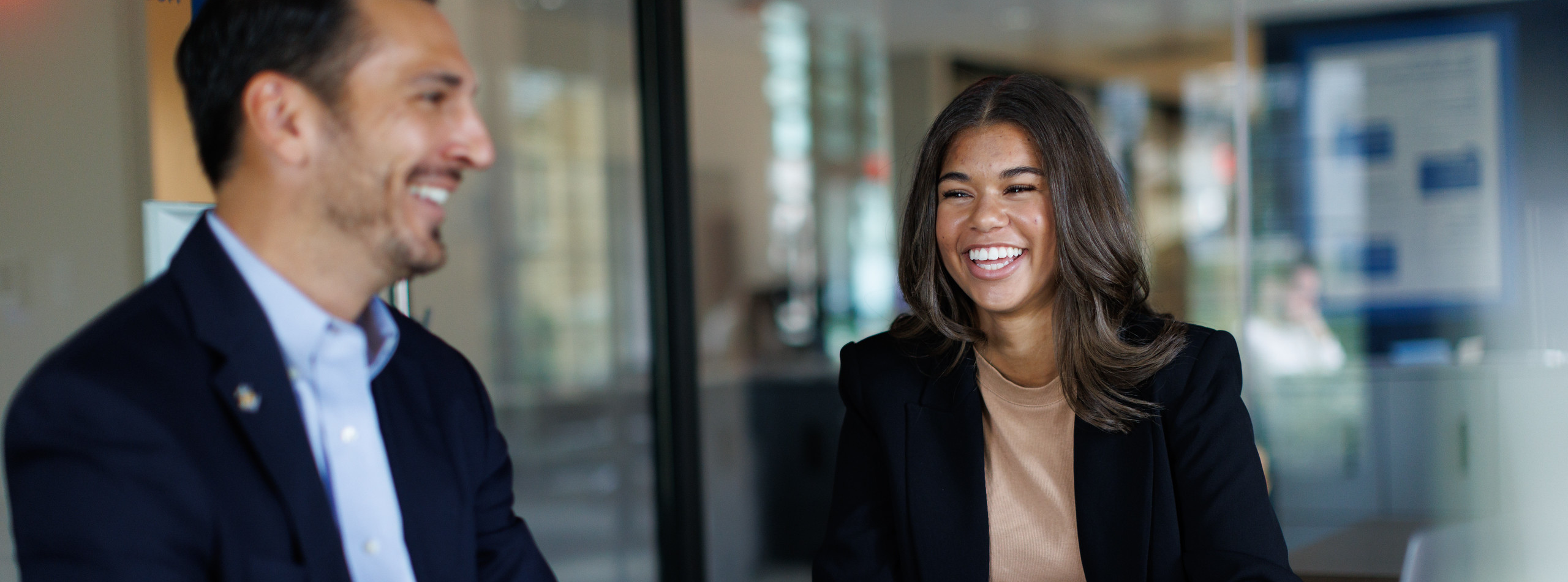 Kaley Klatt smiling and sitting with laptop in office with man in suit. 