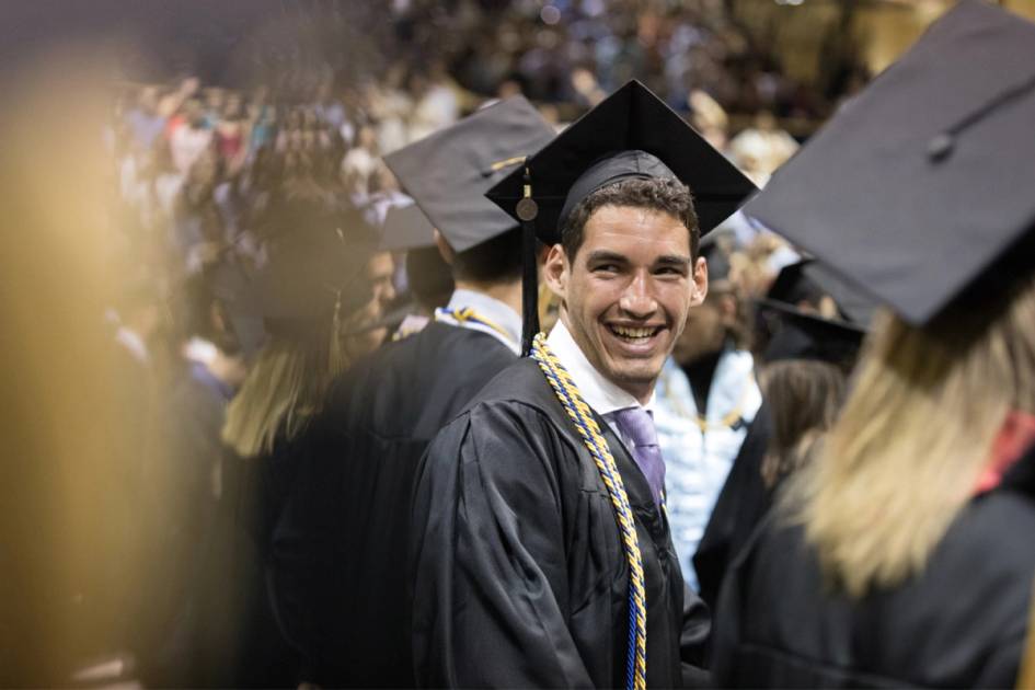 student in cap and gown, turns to smile at friends during the commencement ceremony