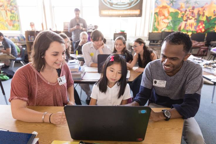 Two college students help an elementary school student practice her coding skills.