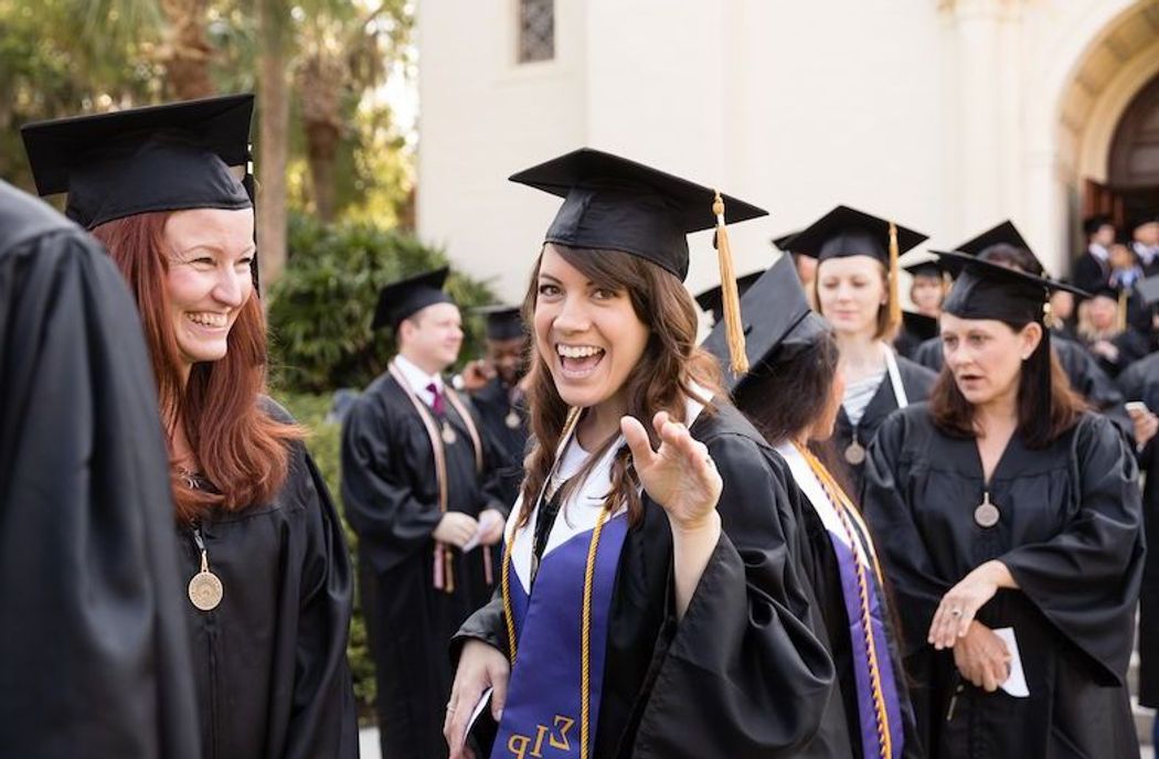 Student in cap and gown smiles and waves