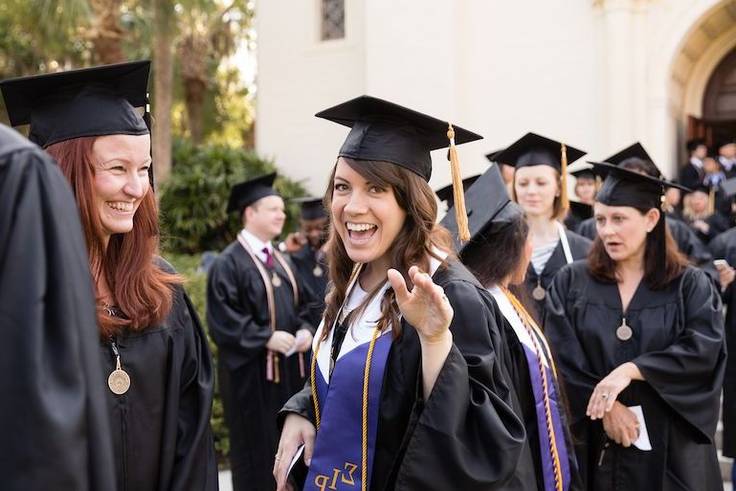 Student in cap and gown smiles and waves