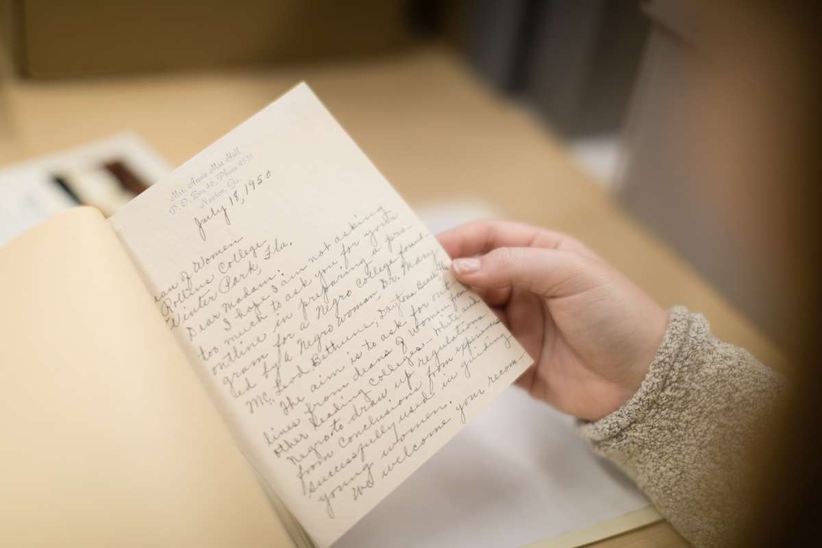 An American History college student is reading an archived card with cursive writing from 1950.