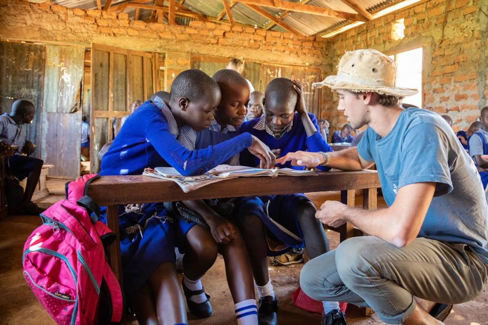 A college student helps three students with their school work in Africa.