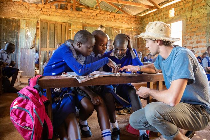 A college student helps three students with their school work in Africa.