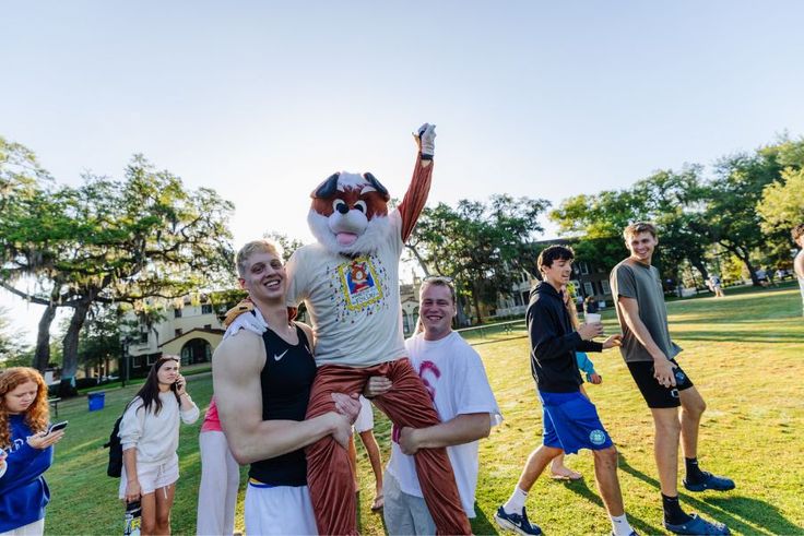 Students celebrate Fox Day outdoors, lifting a costumed mascot.