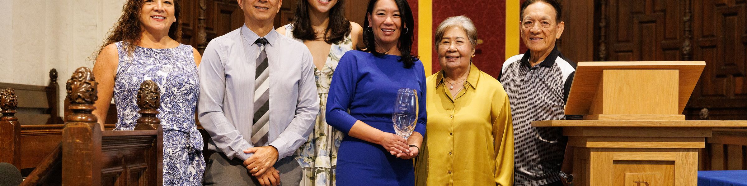 Alumna and family standing in Knowles Chapel as she poses with Alumni Award.