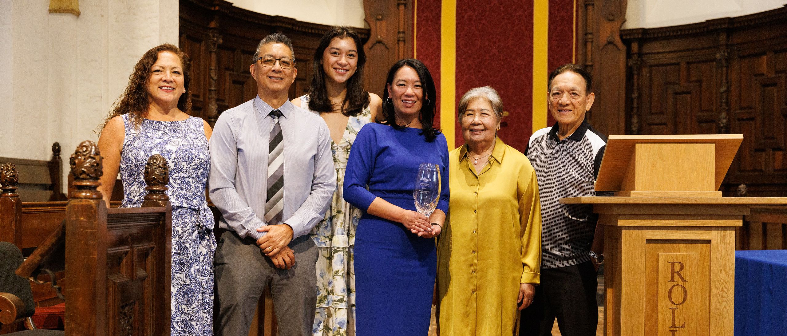 Alumna and family standing in Knowles Chapel as she poses with Alumni Award.