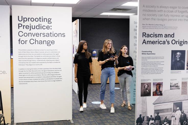 Kaley Klatt ’24, Leah Hornik ’22, and Emily Curran ’22 walk through an exhibit curated by the Take Action Institute