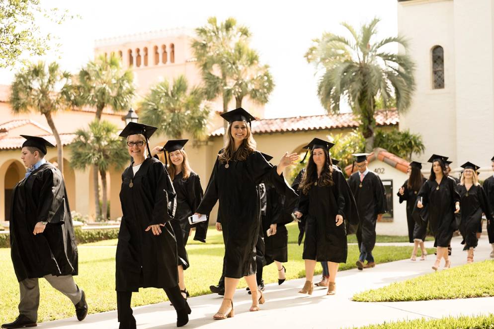 Students in caps and gowns walking past the campus rose garden on graduation day.