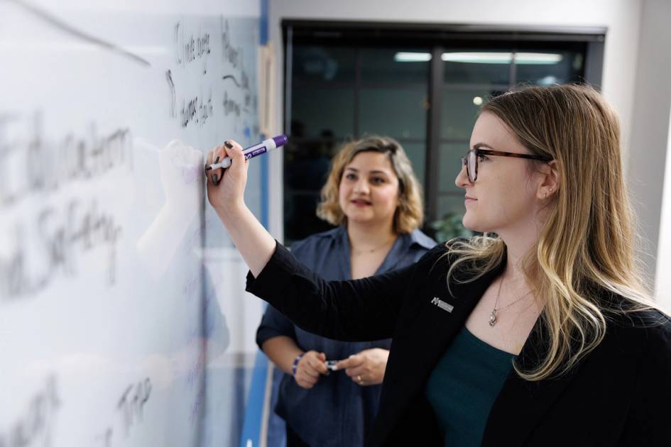 A professor and a student brainstorming and writing ideas on a whiteboard in office.