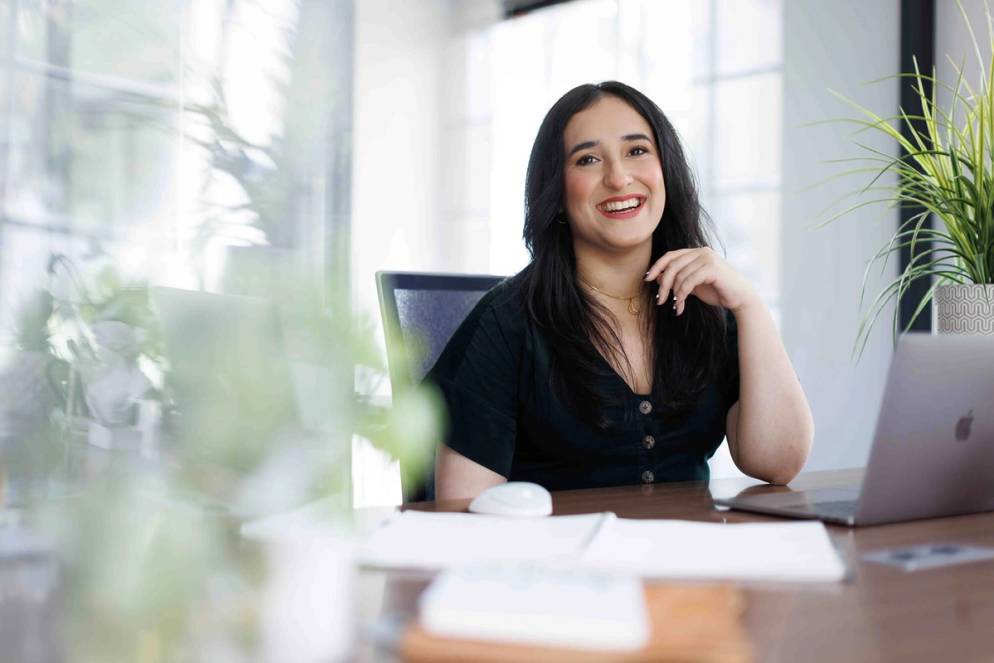 A young professional smiles at the camera from her work desk.