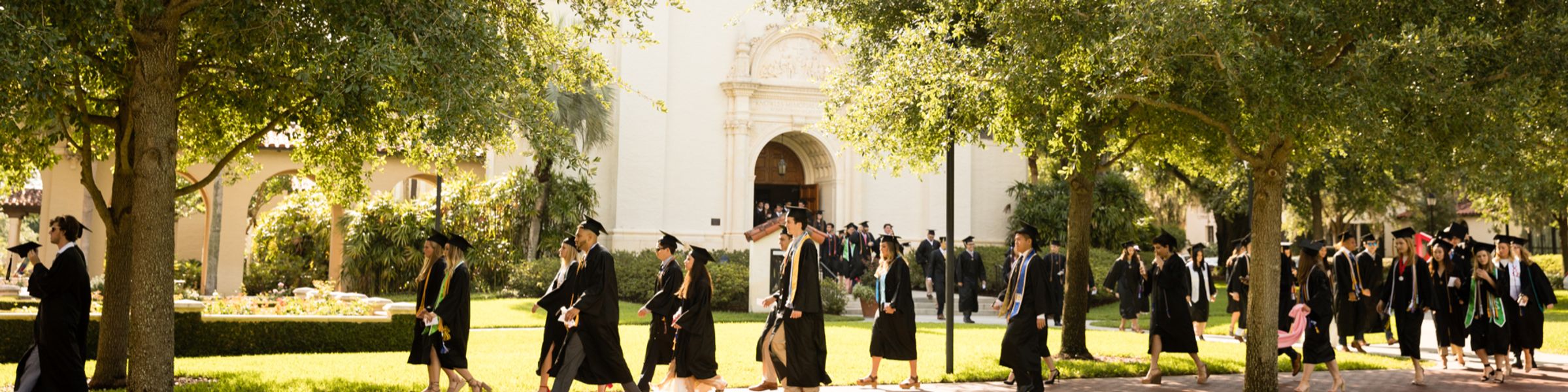 Rollins College graduates walk across campus toward a commencement ceremony..