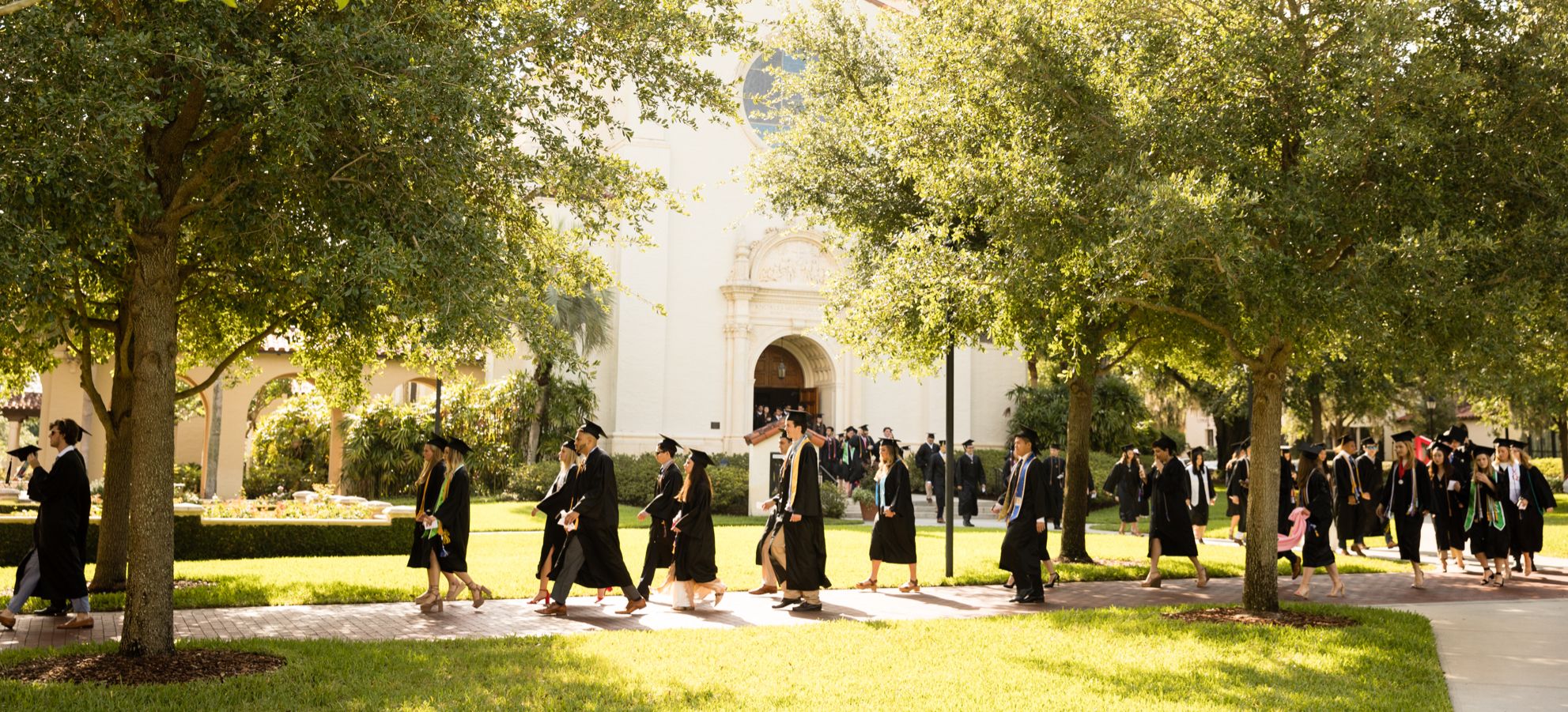 Rollins College graduates walk across campus toward a commencement ceremony..