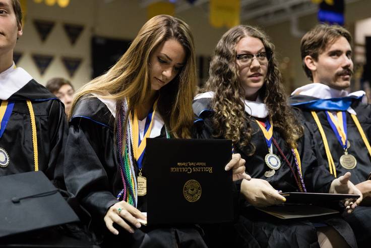 A college graduate looks down at her diploma during a commencement ceremony.
