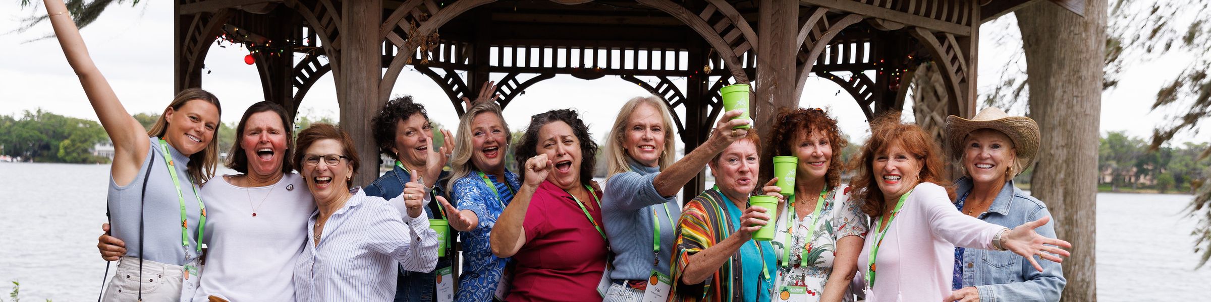 Alumni cheersing at the camera in front of a gazebo along a lake shore.