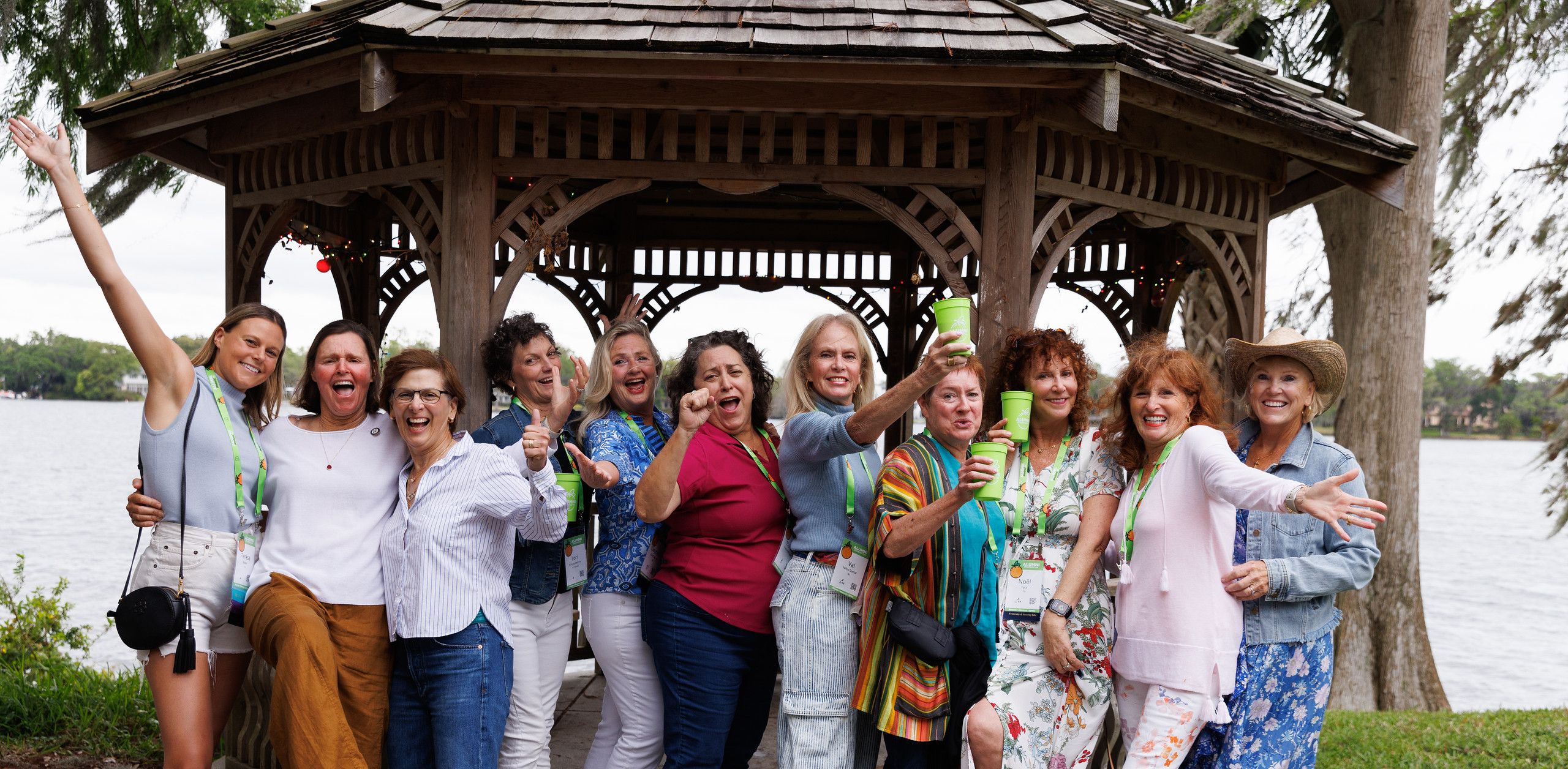 Alumni cheersing at the camera in front of a gazebo along a lake shore.