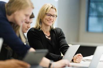A student smiles as a professor explains a concept to a small group of students.