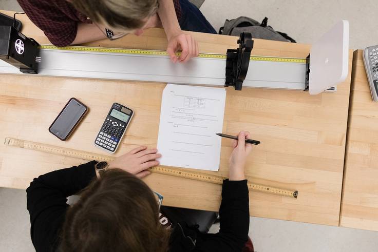 A view from above two students working on a physics problem together seated at a table with a calculator out.