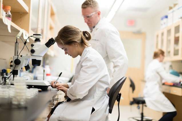 A biology college student writing down observations in the biology lab.