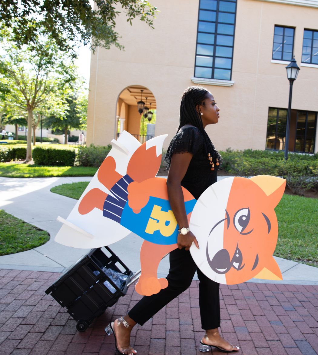 International student working on campus as a social media intern, taking a cut-out of the Fox and merch items out to a campus event