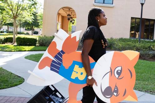 International student working on campus as a social media intern, taking a cut-out of the Fox and merch items out to a campus event