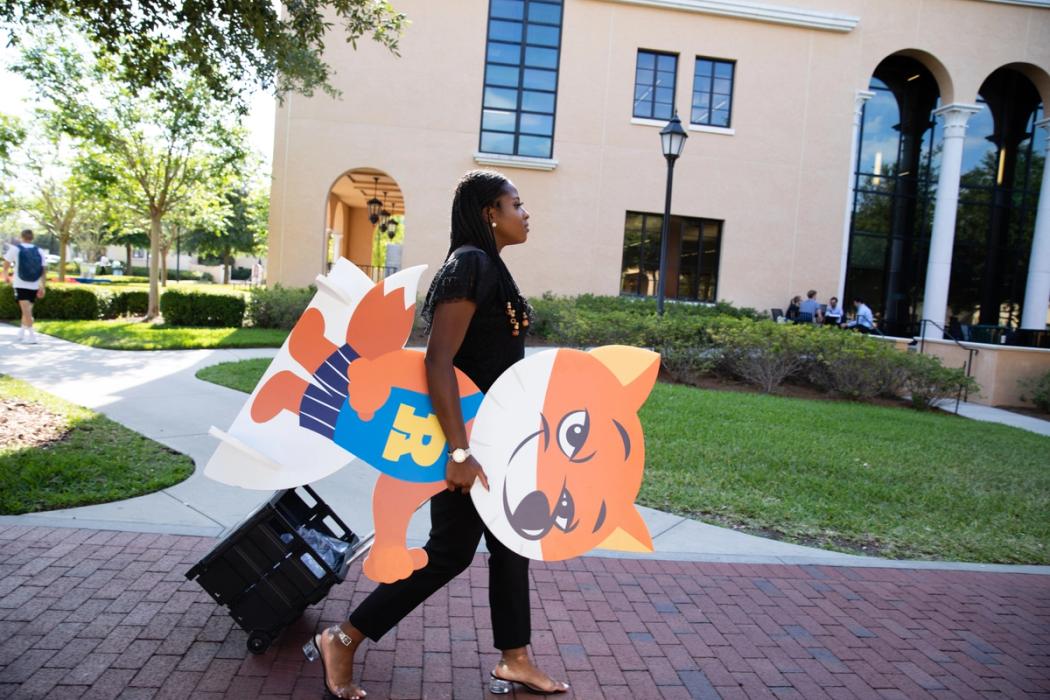 A Rollins student carries a cardboard cut out of the Fox mascot across campus.