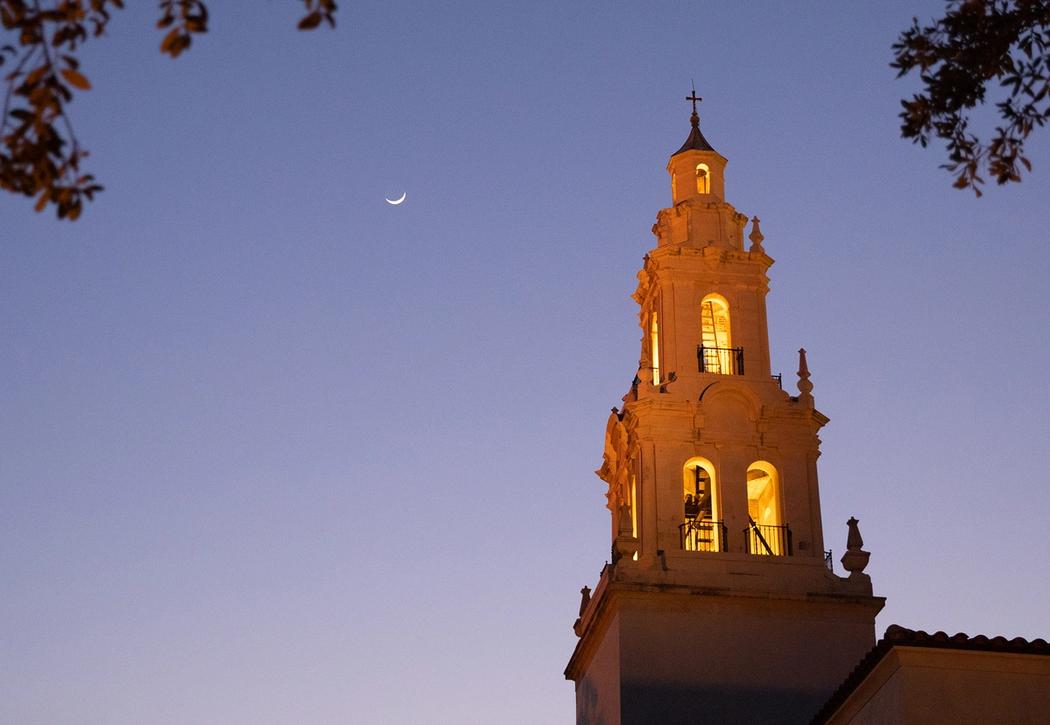 Rollins' Knowles Memorial Chapel's tower lit at dusk with a crescent moon in the sky