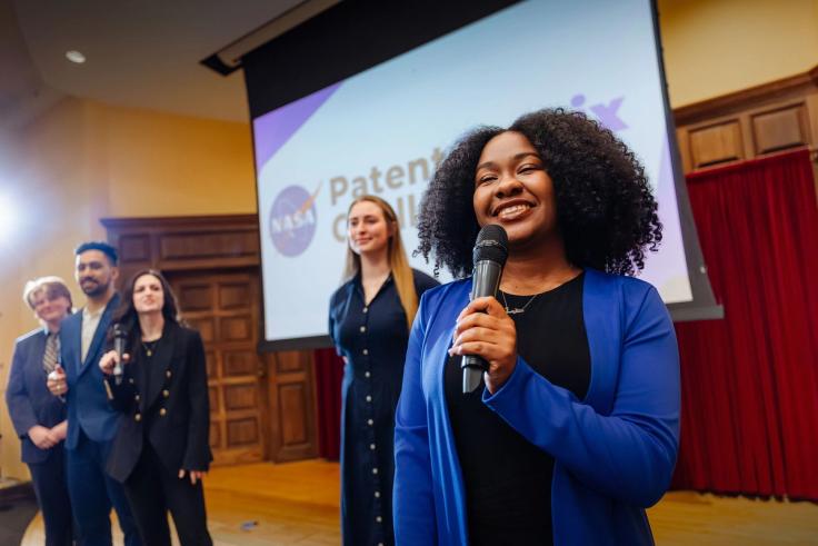 Presenter Xandria Bramble ’25 ’26MBA  speaks into microphone during NASA Patent Challenge event onstage.