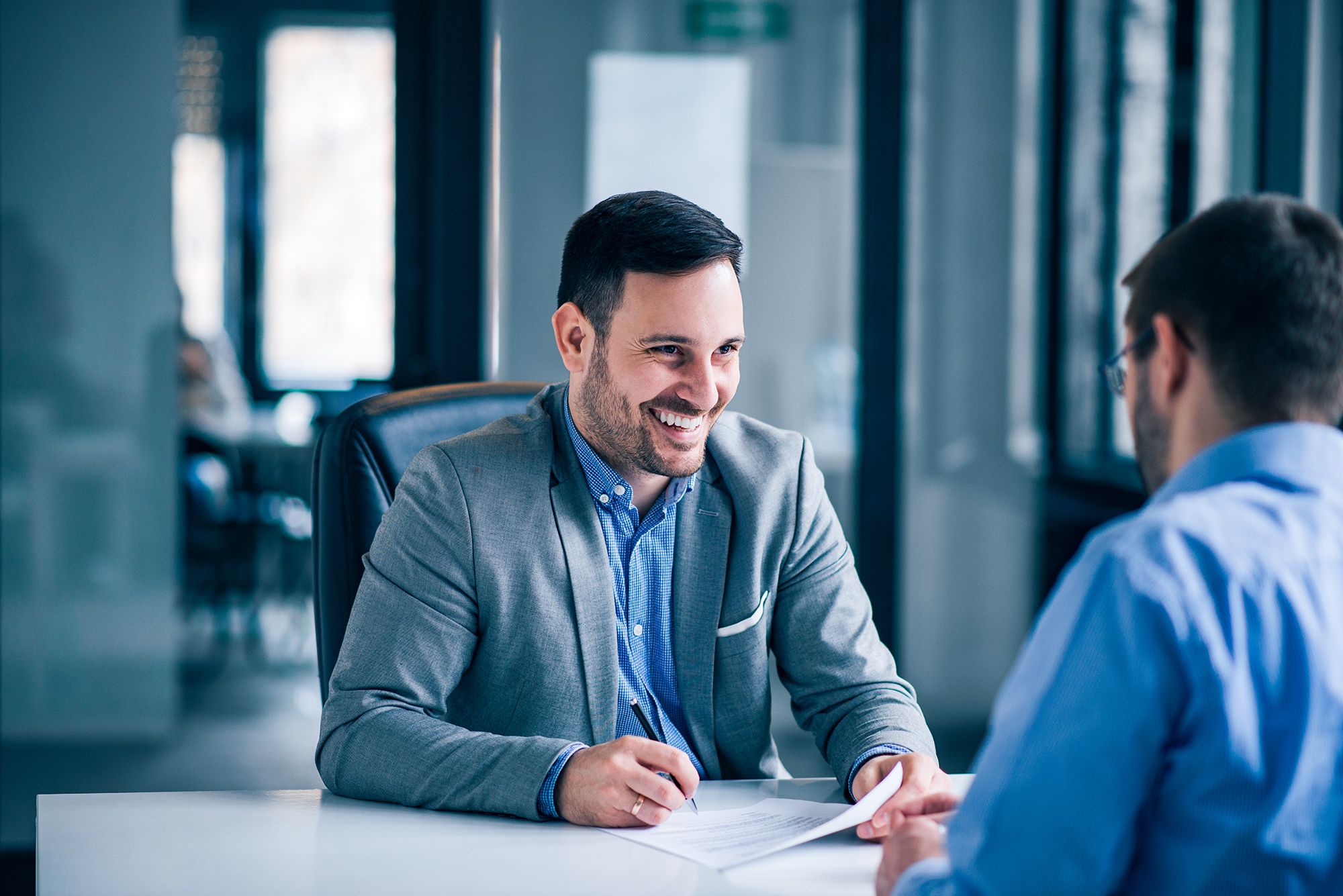 A businessman meets with a client in a glass-walled conference room.