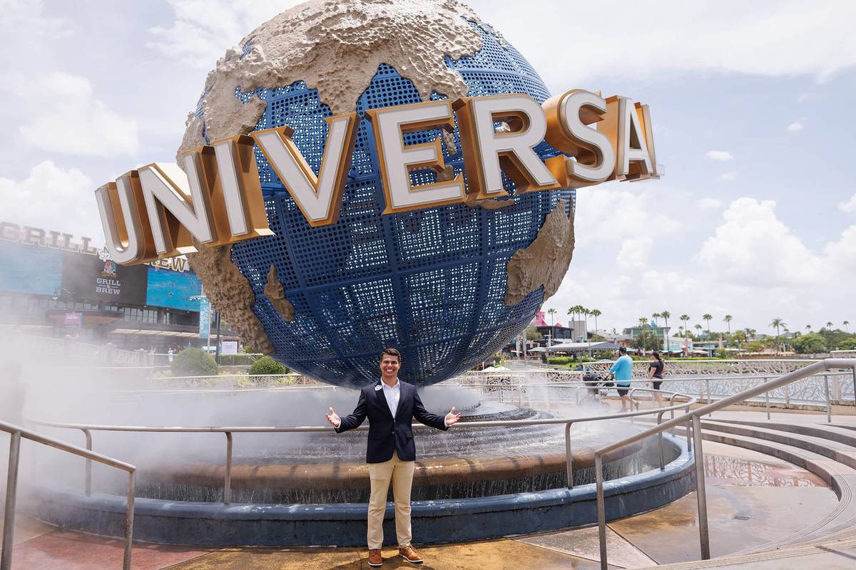 A student in a blazer poses with open arms in front of the rotating Universal Studios globe.