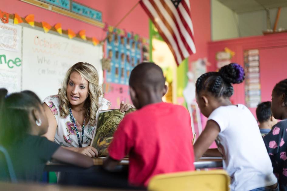 An elementary school teacher reads a book aloud to a group of students in class.