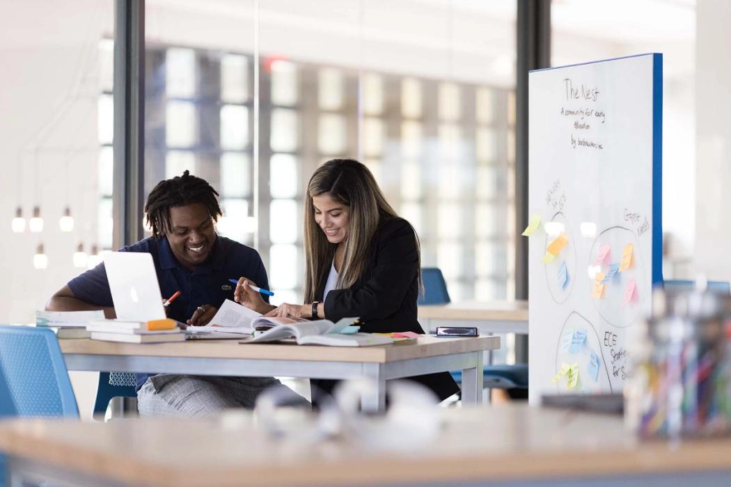 Rollins student and professor work together on a project at the Social Impact Hub, with whiteboard behind them full of notes and sticky notes.