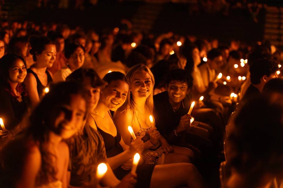 Students with candles sitting together at night, smiling at the camera