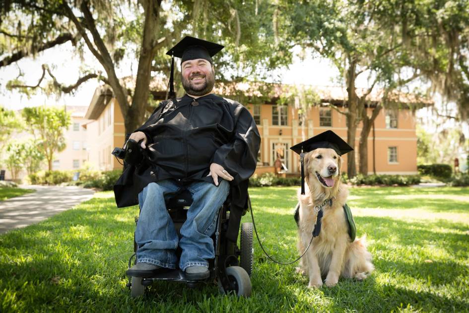 A Rollins grad poses in cap and gown alongside his service dog.