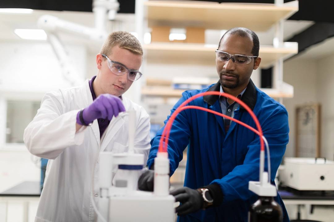 A student professor work side by side in a chemistry lab.