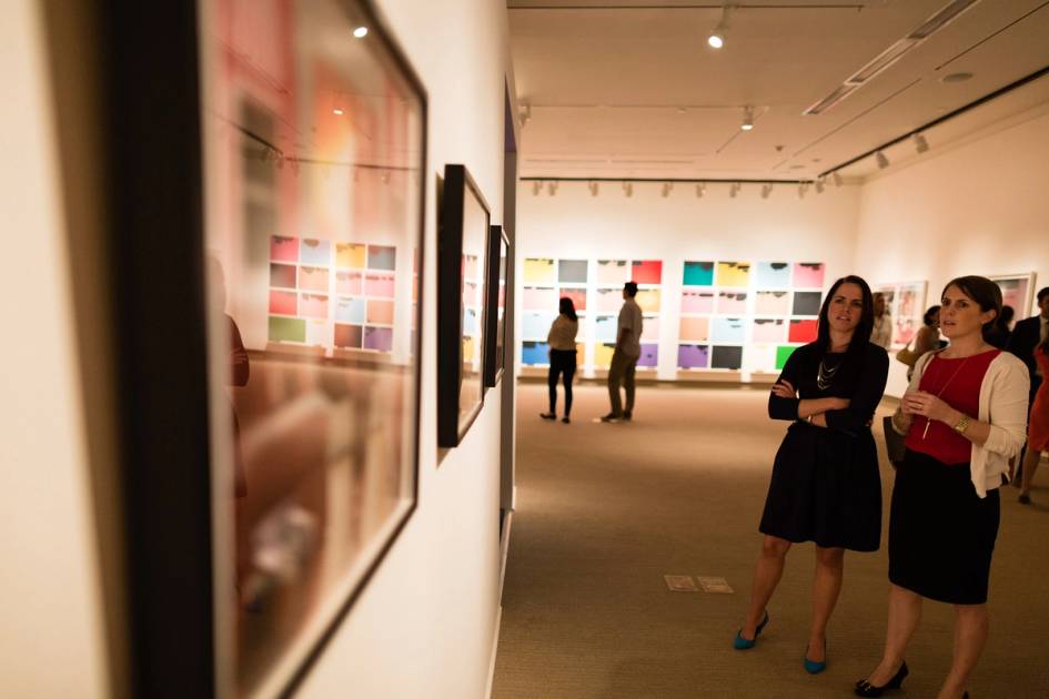 Visitors viewing colorful contemporary artwork in a brightly lit gallery space.