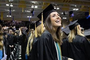 A college graduate smiles at the crowd during a commencement ceremony.