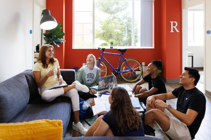 A group of students smile and laugh as they hang out in a residence hall living room at Rollins College.