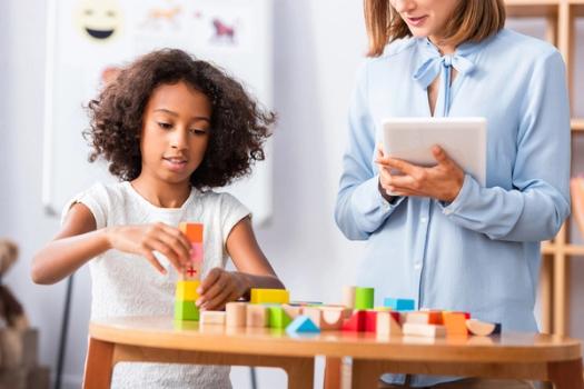 An applied behavior analyst observes a young patient stacking colorful blocks.