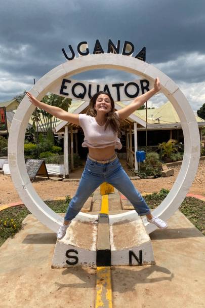 Capri Gutierrez jumping in front of Uganda/Equator sign